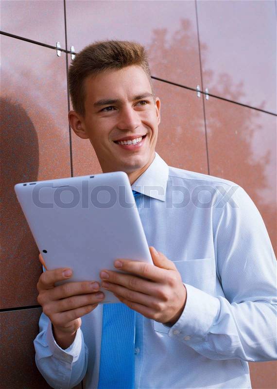 Smiling Businessman Holding Tablet Computer, Looking into the Distance,and Leaning Against Wall, stock photo