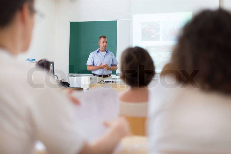 Teacher at university in front of a whiteboard screen. Students listening to lecture and making notes, stock photo