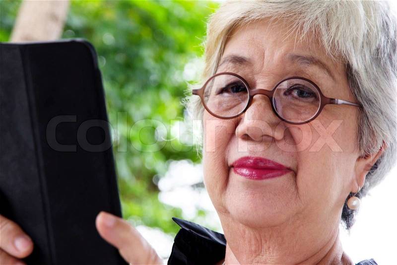 Senior women relaxing at home reading E-book on her tablet, stock photo