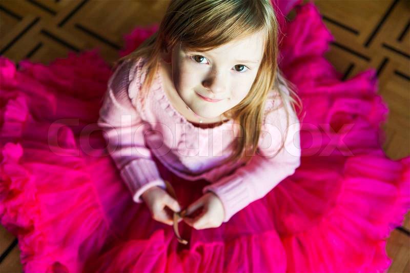 Indoor portrait of a beautiful little girl sitting on a floor in a bright pink skirt tutu, stock photo