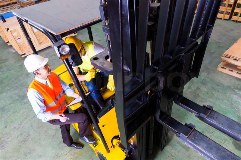 Asian fork lift truck driver discussing checklist with foreman in warehouse , stock photo