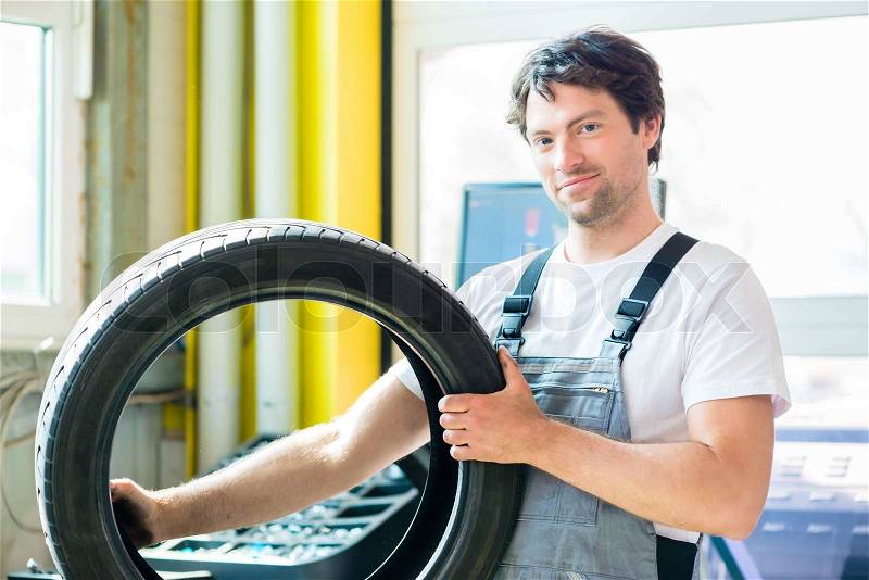 Auto mechanic changing tire in car workshop, stock photo