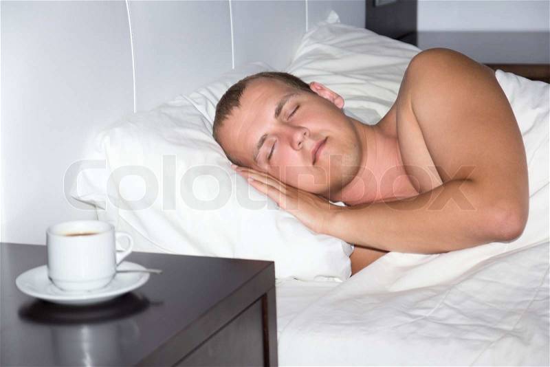 Sleeping man and cup of coffee in bedroom, stock photo