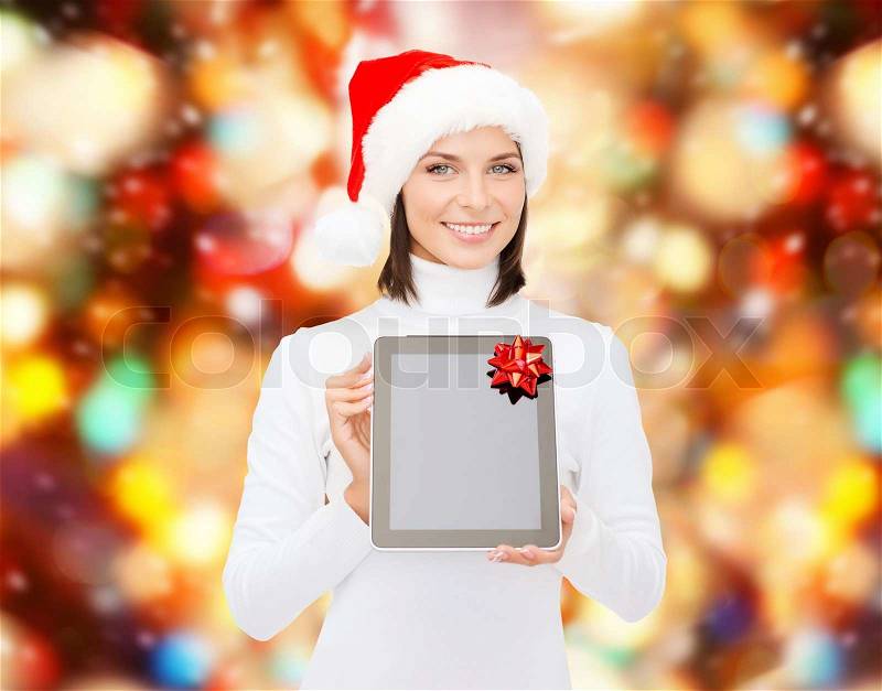 Christmas, technology, present and people concept - smiling woman in santa helper hat with blank screen tablet pc computer over red lights background, stock photo