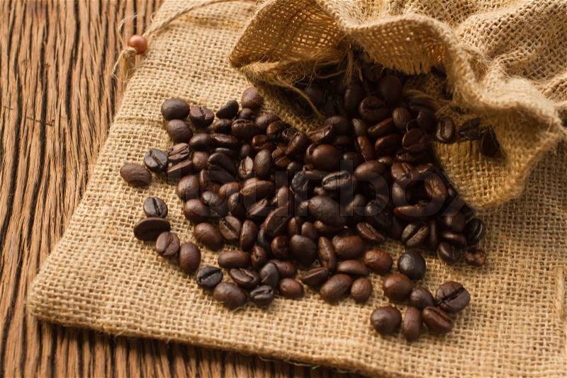 Coffee beans in coffee bag made from burlap on wooden background, stock photo