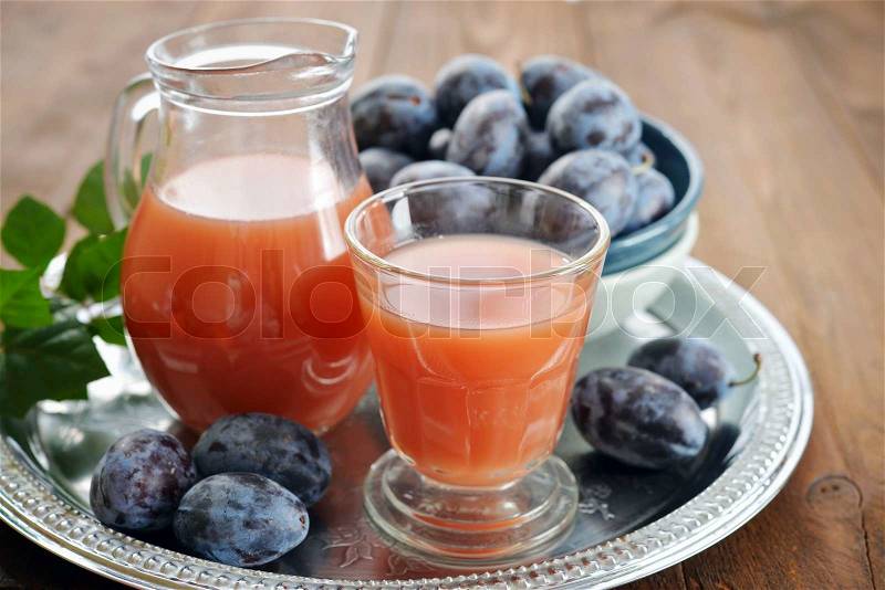 Plum juice in jug and glass with fresh plums on wooden background, stock photo