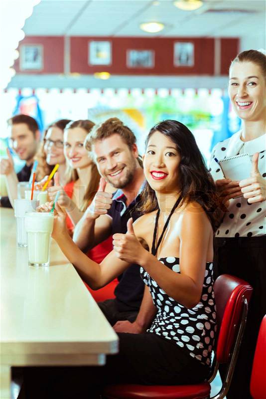 Friends or couples eating fast food and drinking milk shakes on bar in American fast food diner, the waitress is taking orders, stock photo