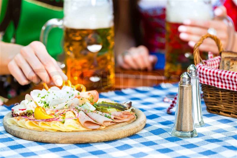 In Beer garden - friends in Tracht, Dirndl and Lederhosen with snacks drinking a fresh beer in Bavaria, Germany, stock photo