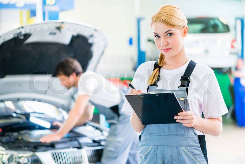 Male and female mechanic team examine car engine with light and checklist in workshop , stock photo