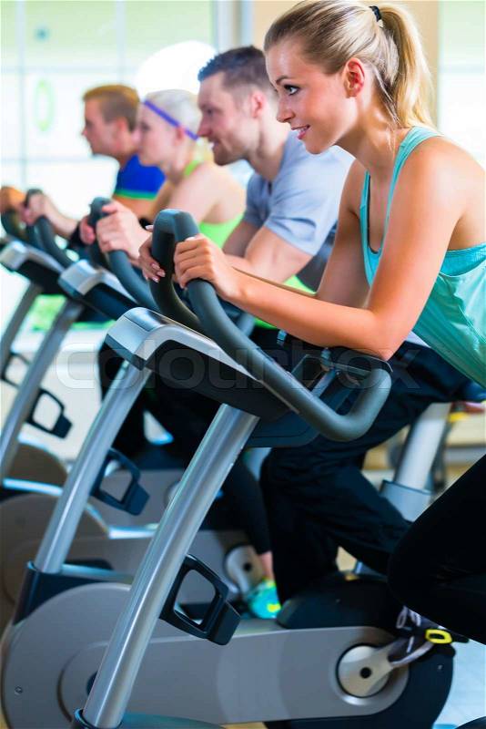Group of fitness people in sport gym spinning on bicycles, stock photo