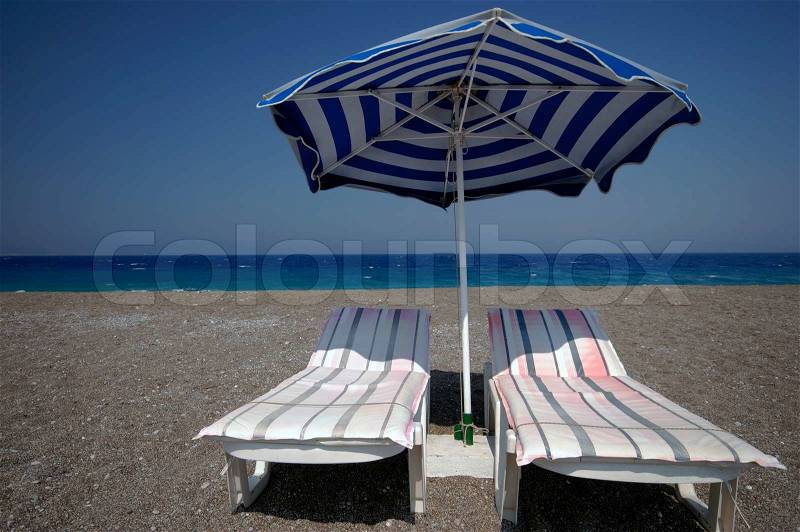 One umbrella and two chairs on the beach close to the sea, stock photo