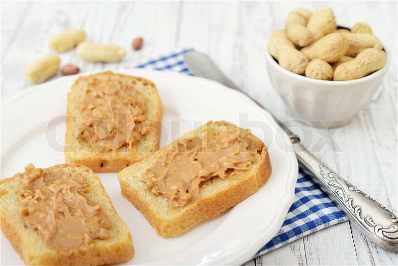 Peanut butter sandwich on plate with nuts on wooden background, stock photo