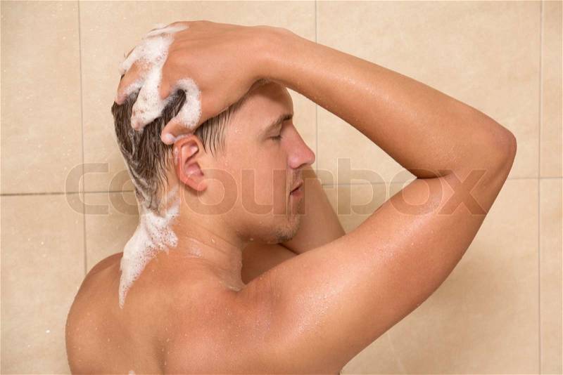 Young attractive man washing his hair in shower, stock photo
