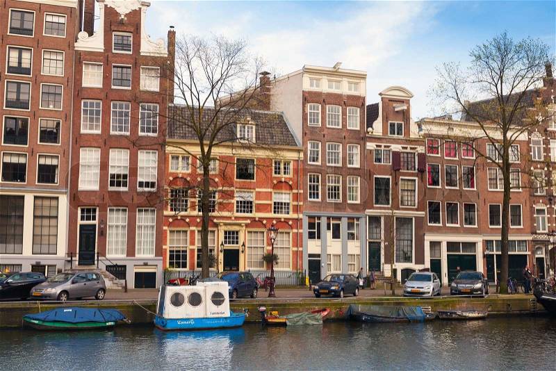 AMSTERDAM, NETHERLANDS - MARCH 19, 2014: Colorful houses along the canal embankment in spring day. Ordinary people are on the coast, stock photo