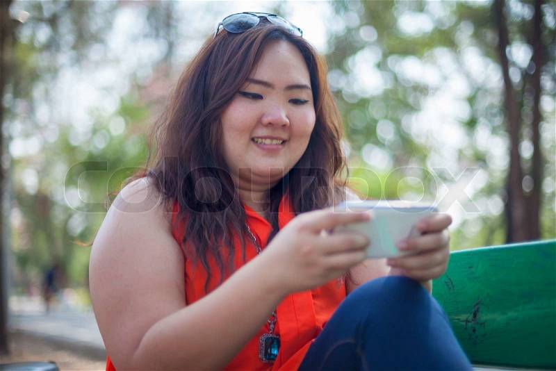 Happy fatty asian woman using mobile phone outdoor in a park, stock photo