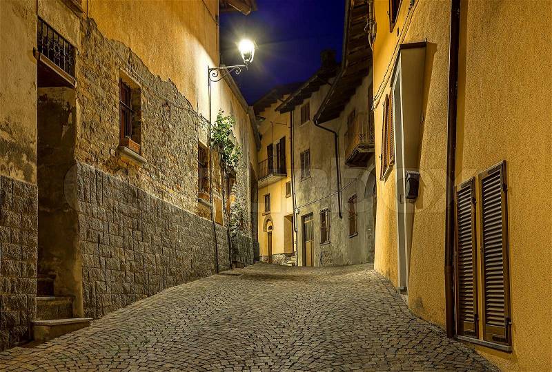 Narrow cobbled street among old houses at night in town of Barolo, Italy, stock photo