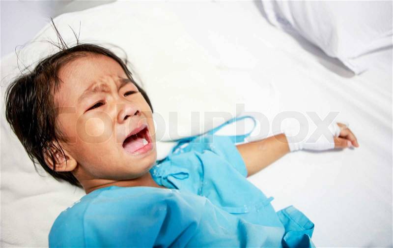 Sick little girl crying in hospital bed, stock photo