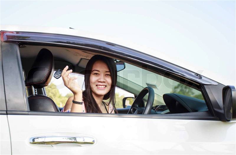 Asian car driver woman smiling showing new car keys and car. Mixed-race Asian and Caucasian girl, stock photo