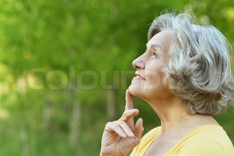 Nice smiling old woman on the green leaves background, stock photo