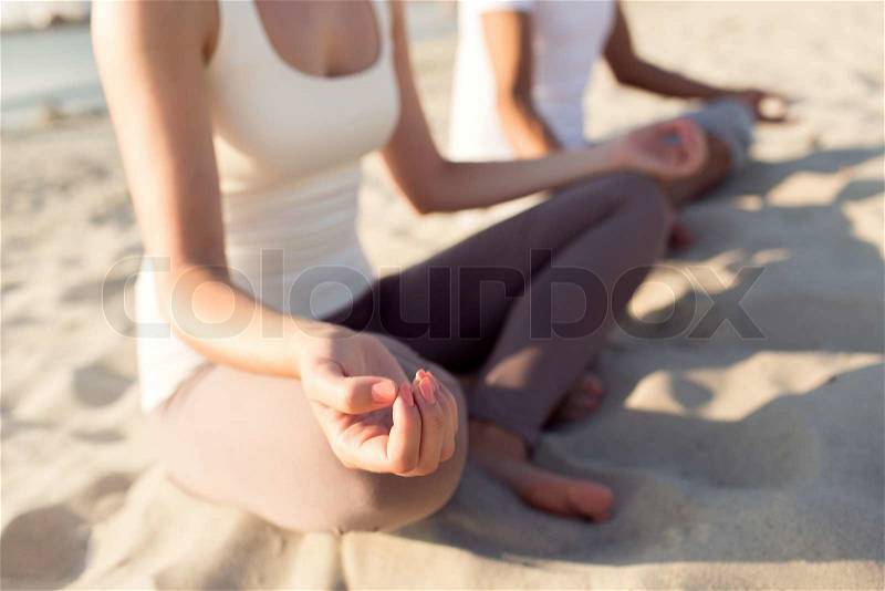 Fitness, sport, people and lifestyle concept - close up of couple making yoga exercises sitting on pier outdoors, stock photo