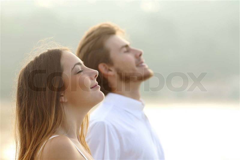 Profile of a couple of man and woman breathing deep fresh air together at sunset , stock photo