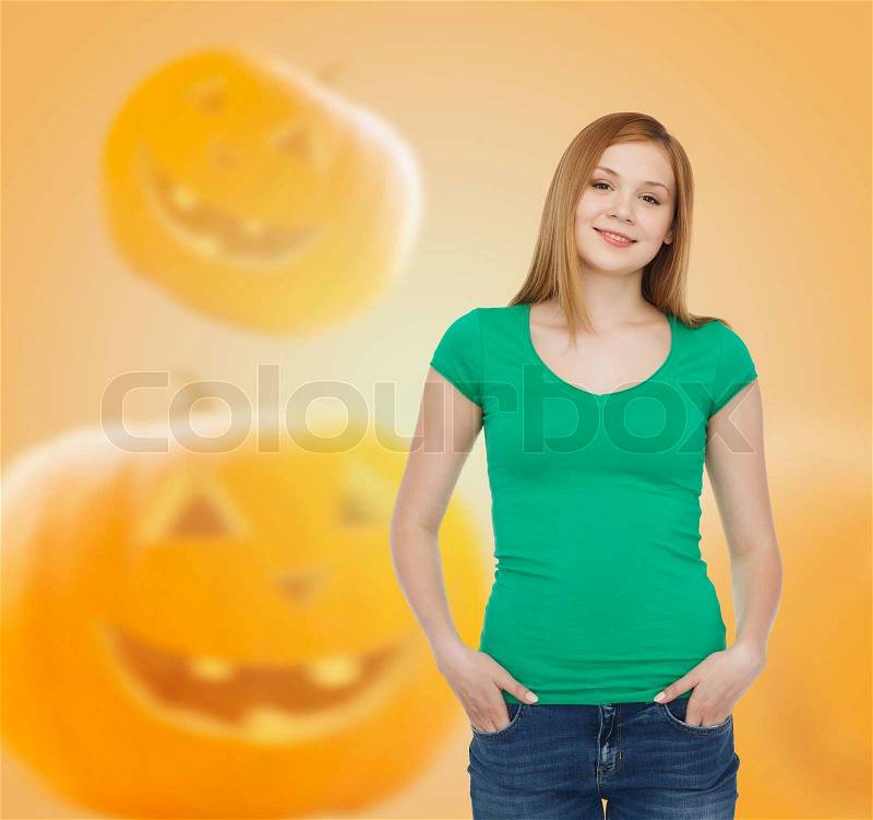 Holidays, advertisement and people concept - smiling young woman in blank green t-shirt over halloween pumpkins background, stock photo