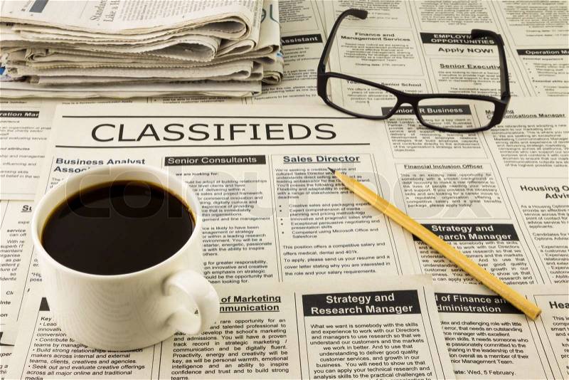 Fake classifieds ads on newspaper place on table with glasses, pencil and a cup of coffee, stock photo
