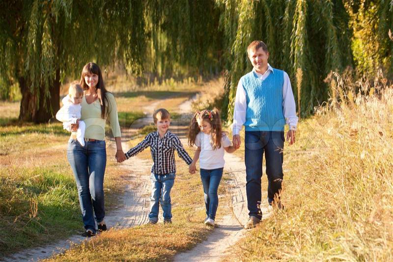 Big happy family walking on the road in the park. Father, mother, son, daughter and baby holding hands and going together. Family Ties concept, stock photo