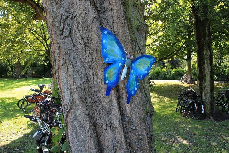 Selfmade blue butterfly on the trunk and many bikes standing in the park in summertime, stock photo