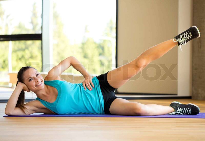 Fitness, sport, training and lifestyle concept - smiling woman doing exercises on mat in gym, stock photo