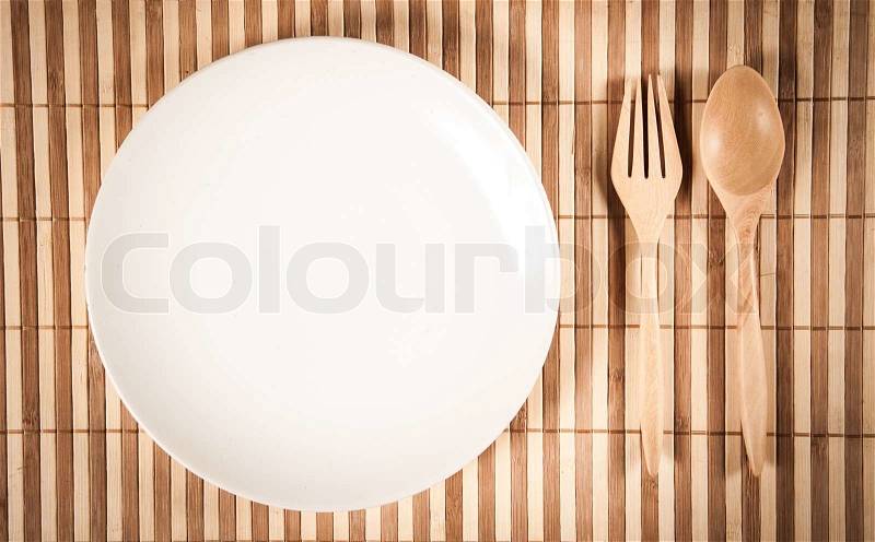 Wooden spoon and fork and empty dish display on bamboo napery, stock photo