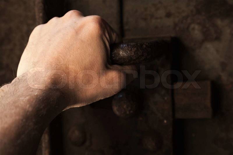 Male hand pull the handle of old rusted prison metal door with big lock, stock photo