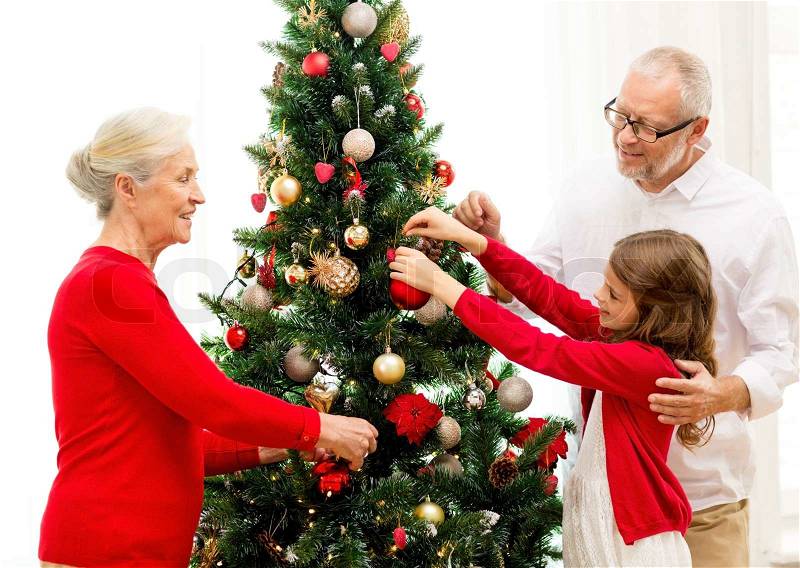 Family, holidays, generation and people concept - smiling family decorating christmas tree at home, stock photo
