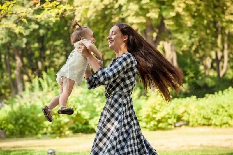 Beautiful mother holding baby girl on hands and spinning around at park, stock photo
