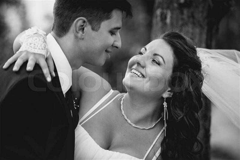 Closeup monochrome portrait of bride and groom embracing and laughing at windy day, stock photo