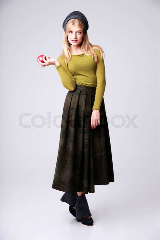 Full length portrait of a serious woman standing with apple on gray background, stock photo