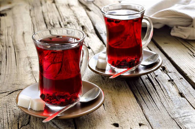 Red hibiscus tea in two glass cups on weathered wooden background with sugar cubes in brown saucers, stock photo
