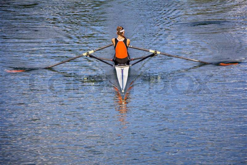 The woman rower in a boat, rowing on the tranquil lake , stock photo