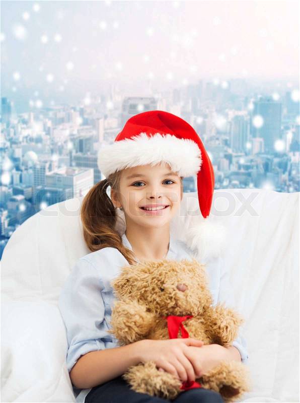 Holidays, presents, christmas, childhood and people concept - smiling little girl with teddy bear toy over snowy city background, stock photo