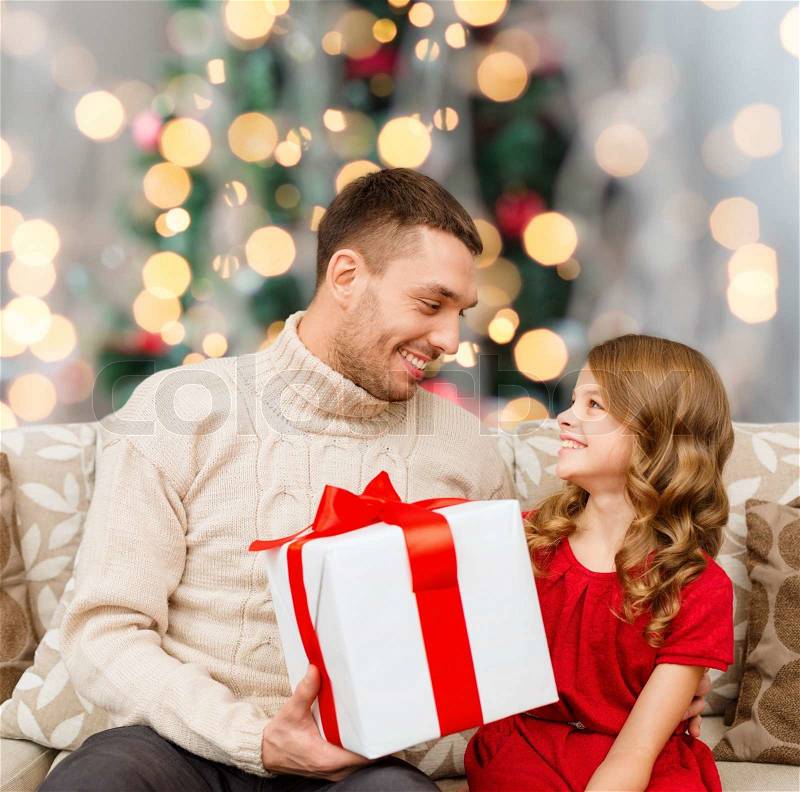 Family, holidays and people concept -smiling father and daughter with gift box over living room and christmas tree background, stock photo
