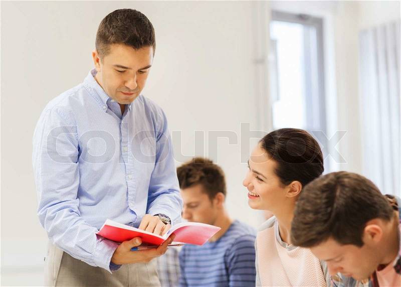Education, high school, teamwork and people concept - group of smiling students and teacher with notebook in classroom, stock photo