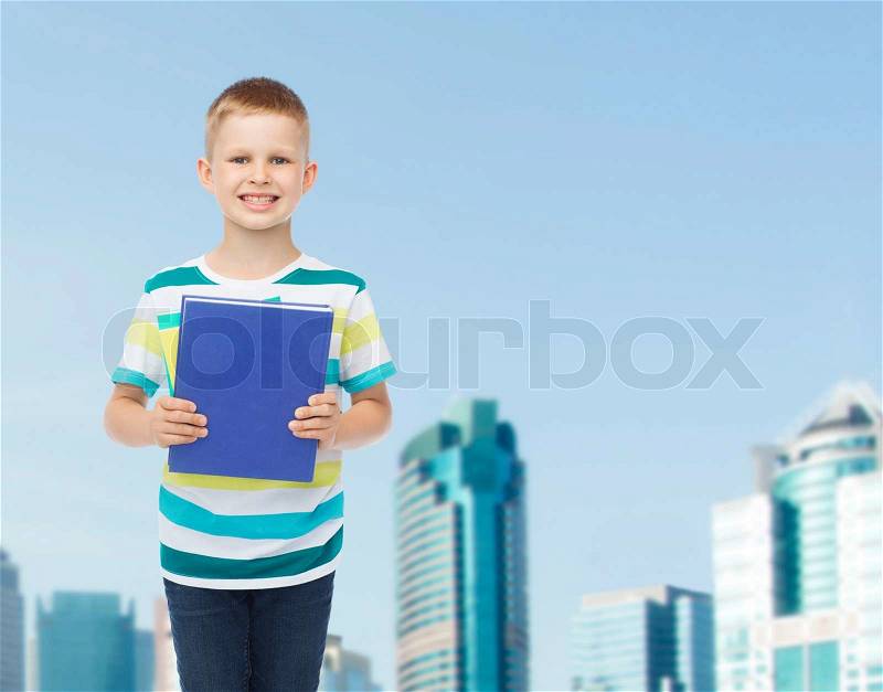 Education, childhood and school concept - smiling little student boy with blue book over city background, stock photo