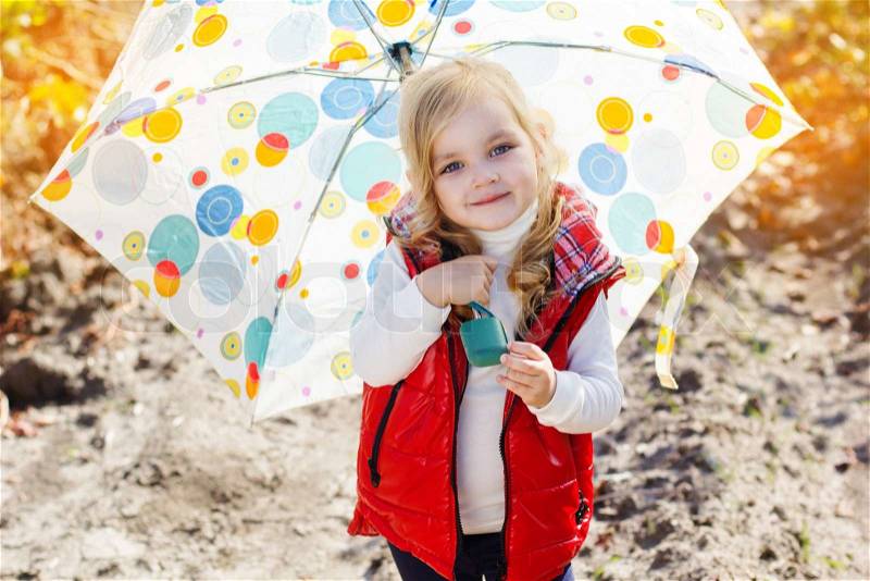 Smiling little girl with umbrella is wearing warm red vest and boots walking on the vineyard, stock photo