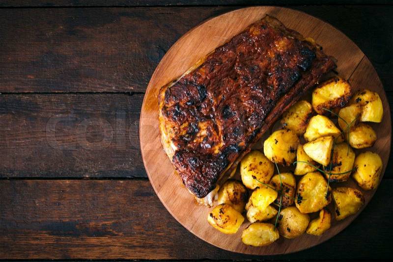 Baked potatoes and beef ribs in bbq sauce from above on wooden background.Blan space on the left side , stock photo