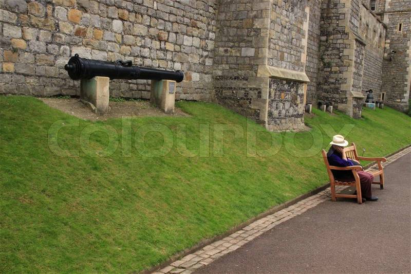 The single man is sleeping on the bench and behind him a big cannon in summertime in Windsor Castle in England, stock photo