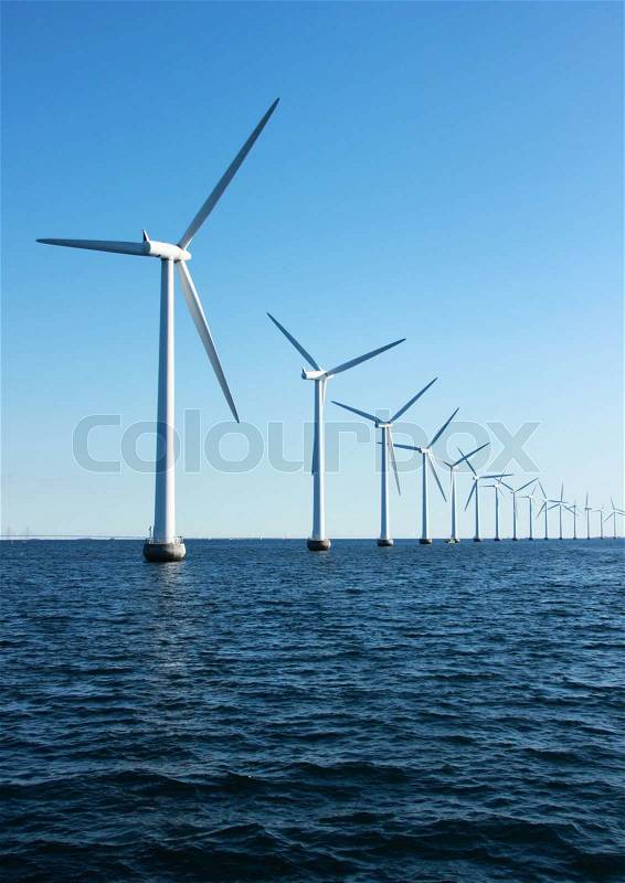 Vertical perspective line of ocean windmills with dark water and sky, stock photo