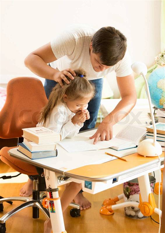 Young father angry at daughter doing homework, stock photo