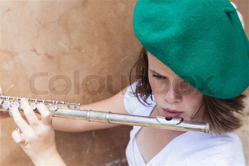 A young girl in a green beret and white shirt sits against a cream wall, stock photo