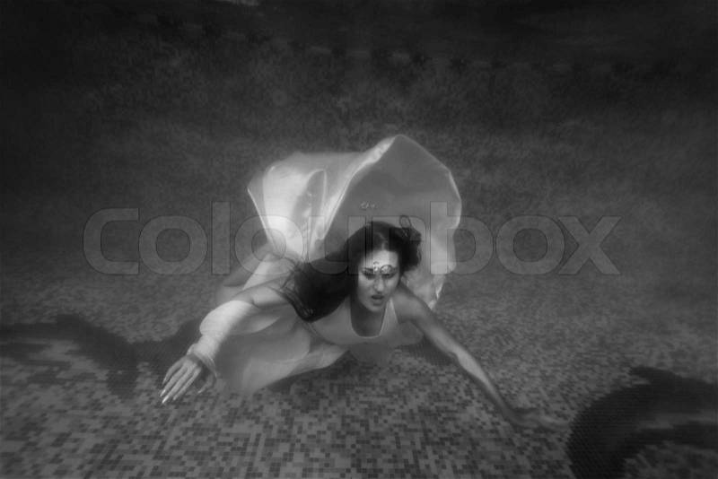 Black and white shot of terrified woman in dress drowning at pool, stock photo