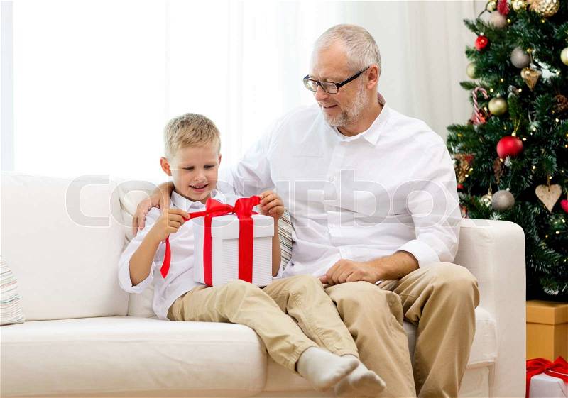 Family, holidays, generation, christmas and people concept - smiling grandfather and grandson with gift box sitting on couch at home, stock photo